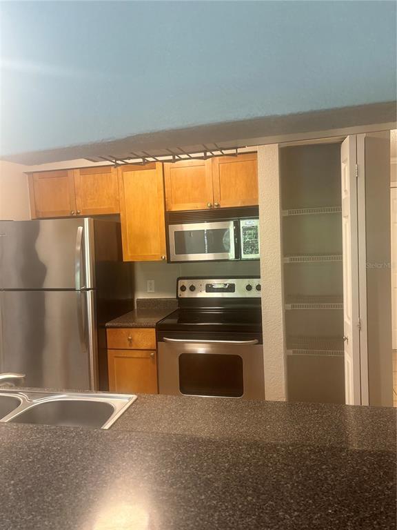 A kitchen features stainless steel appliances, wood cabinets, a dark countertop, and an open pantry — 10100 SAILWINDS BOULEVARD N UNIT 206, LARGO, FL