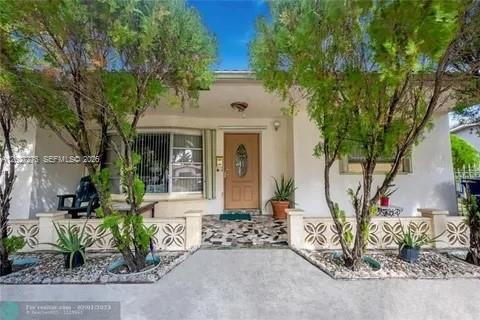 The exterior of a single-story house features a front porch, a wooden door, and landscaping — 1109 NE 4th Ct, Hallandale Beach FL 33009, HALLANDALE BEACH, FL