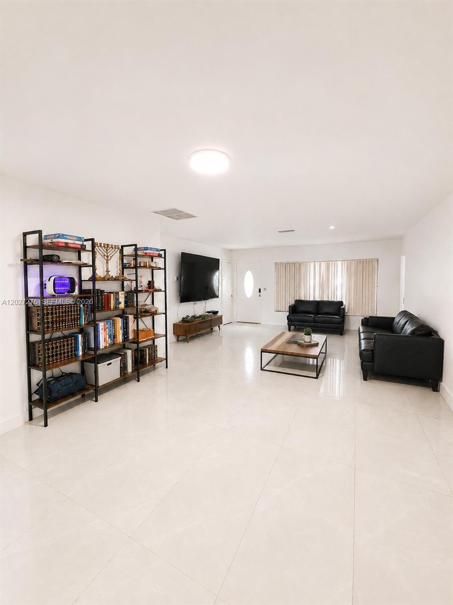 A living room features white tile floors, black leather furniture, and a large metal bookshelf — 1109 NE 4th Ct, Hallandale Beach FL 33009, HALLANDALE BEACH, FL