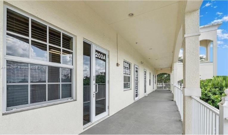 An exterior walkway with white walls, glass doors, and windows leads along a commercial building — 100 N State Road 7 # 203A, Margate FL 33063, MARGATE, FL