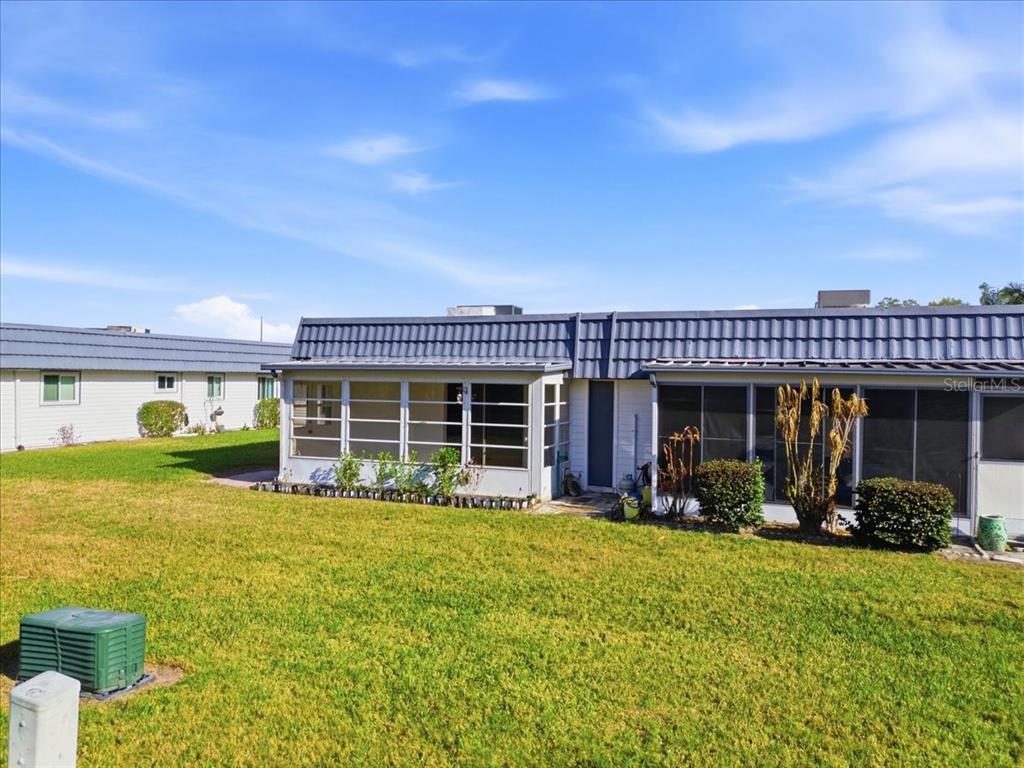 The exterior of a single-story house features a metal roof and a screened-in porch — 205 ANDOVER PLACE N UNIT 119, SUN CITY CENTER, FL