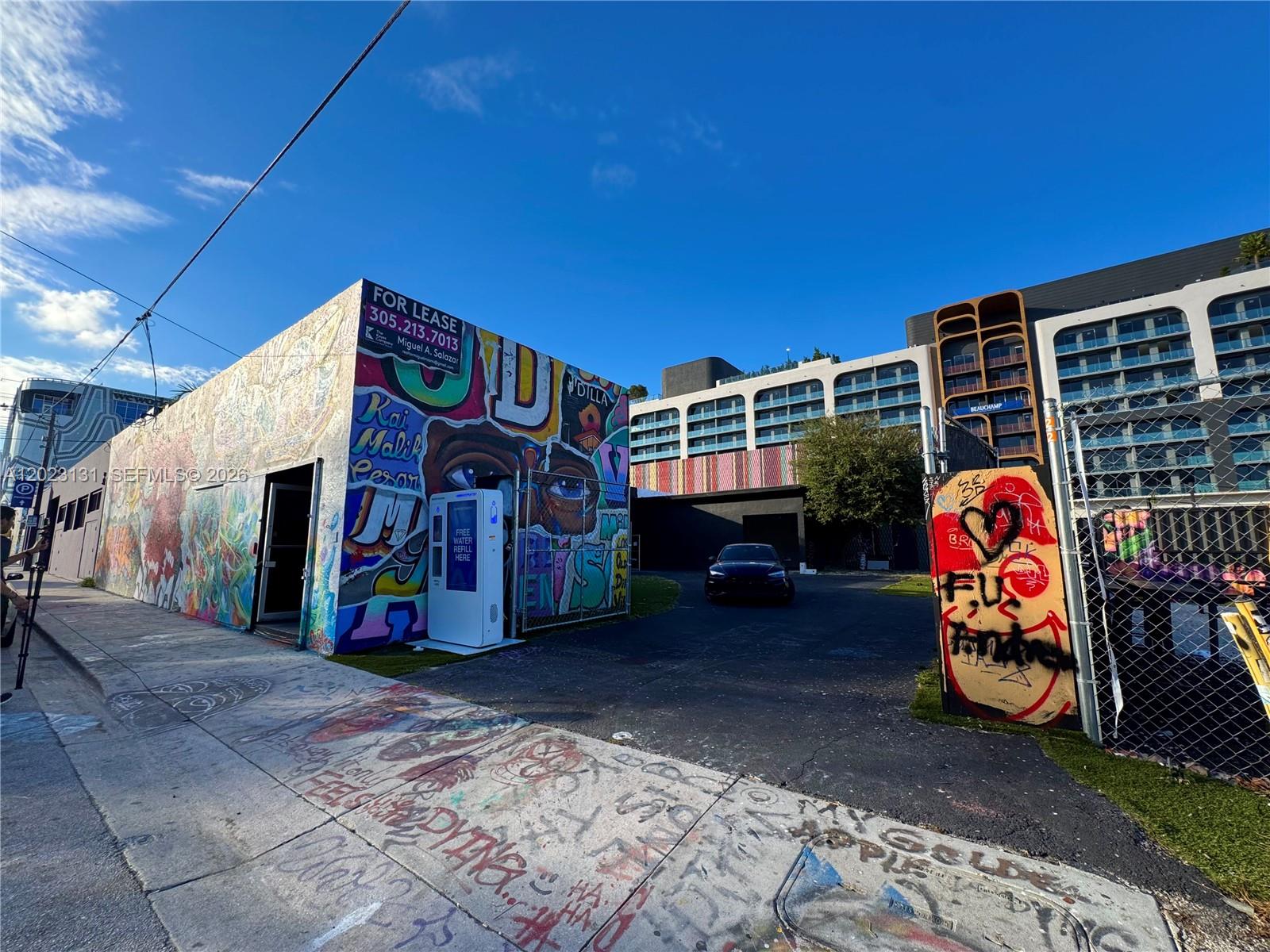A graffiti-covered building exterior stands next to a parking lot with a modern apartment complex — 239 NW 26th St, Miami FL 33127, MIAMI, FL