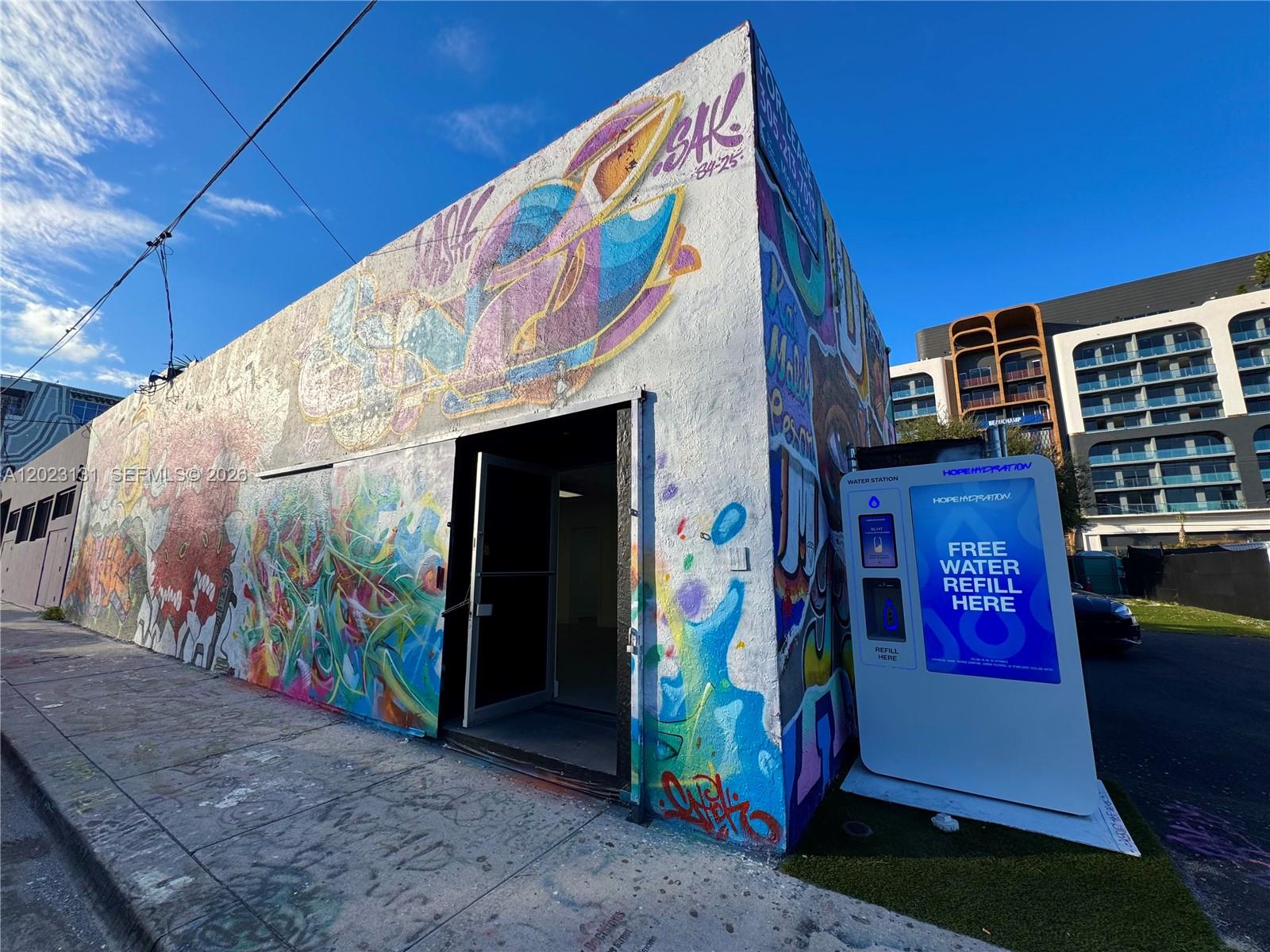 An exterior view of a graffiti-covered building with an open door and a water station — 239 NW 26th St, Miami FL 33127, MIAMI, FL