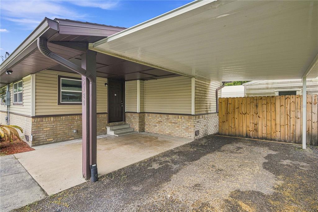 A house exterior features a covered carport, tan siding, brick accents, and a wooden fence — 5420 NE 25TH AVENUE, OCALA, FL
