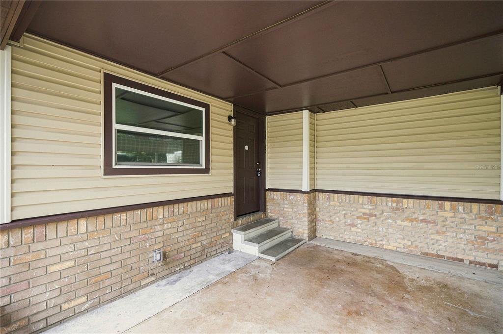 A covered concrete porch features tan vinyl siding, a brick base, and a brown door — 5420 NE 25TH AVENUE, OCALA, FL