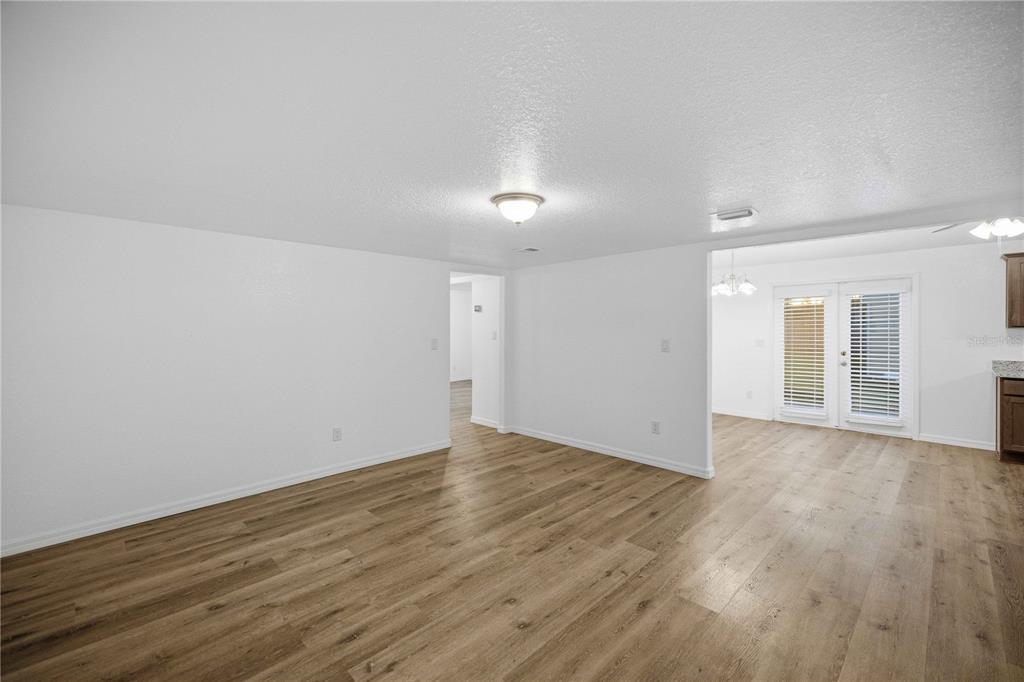 A spacious room with light wood-look flooring, white walls, and a view into a dining area — 5420 NE 25TH AVENUE, OCALA, FL