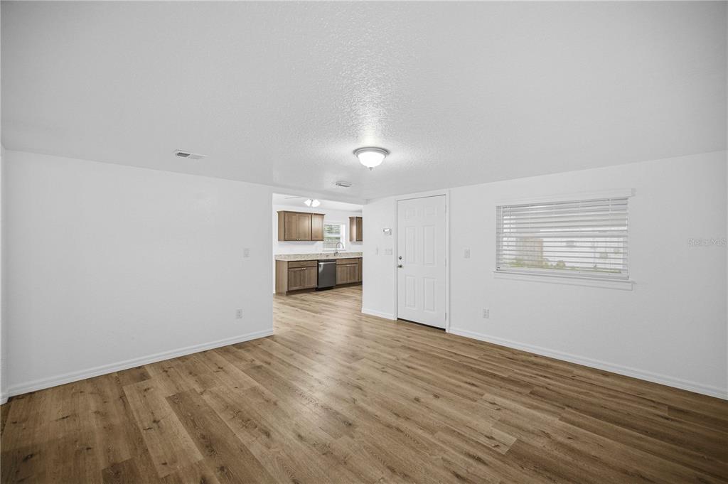 An open-concept living area with light wood-look flooring leads into a kitchen with wood cabinets — 5420 NE 25TH AVENUE, OCALA, FL
