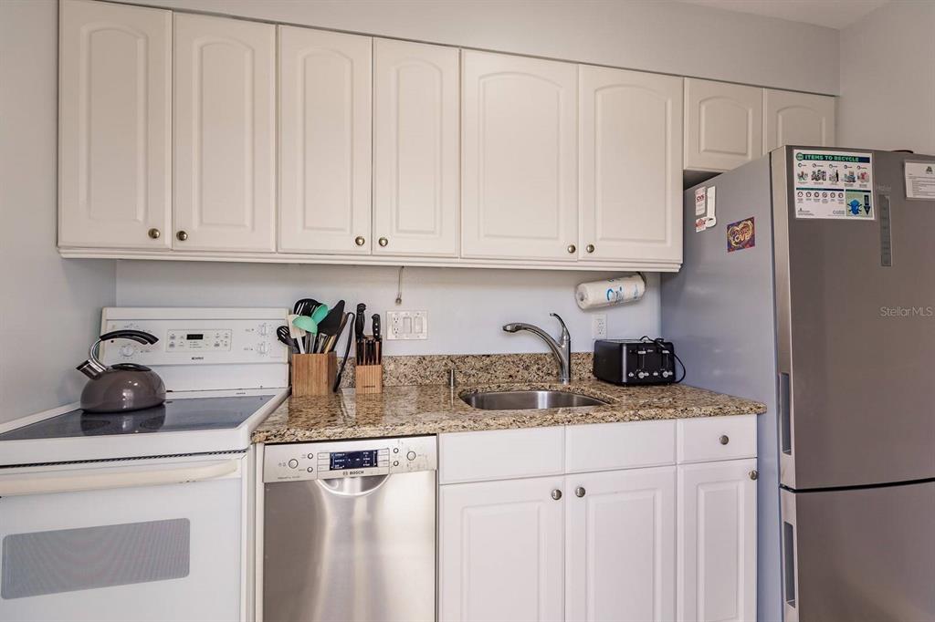 A kitchen features white cabinets, granite countertops, a stainless steel dishwasher, and a stainless refrigerator — 6020 MIDNIGHT PASS ROAD UNIT 4, SARASOTA, FL