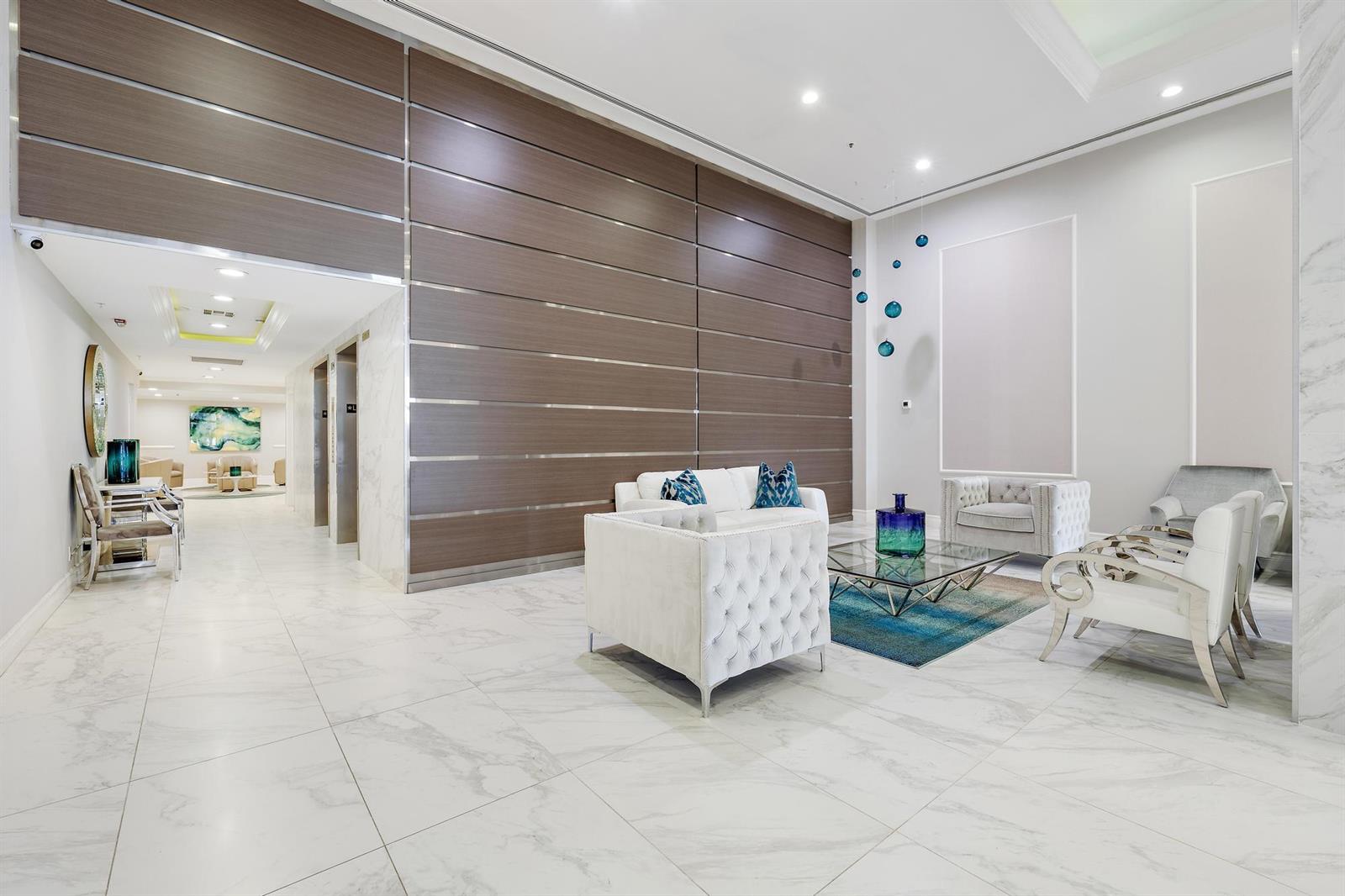 A modern lobby features white marble floors, a wood-paneled accent wall, and plush white seating — 5280 N Ocean Drive # 8b, Riviera Beach FL 33404, RIVIERA BEACH, FL