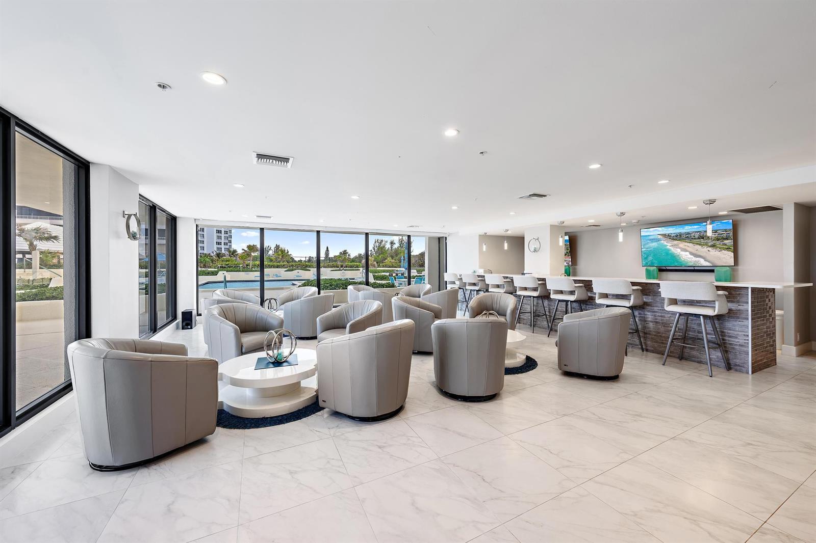A modern lounge features gray leather armchairs, a bar with stools, and floor-to-ceiling windows — 5280 N Ocean Drive # 8b, Riviera Beach FL 33404, RIVIERA BEACH, FL