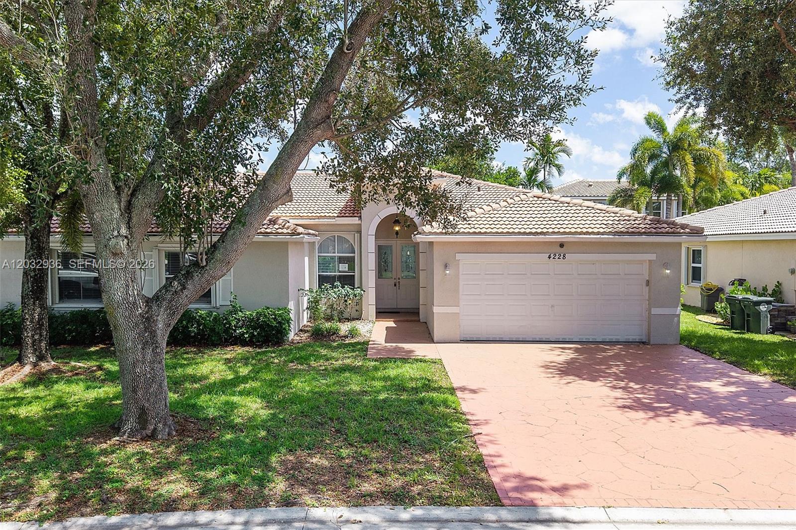 A single-story house features a tiled roof, a two-car garage, and a large front tree — 4228 NW 41st Ln, Coconut Creek FL 33073, COCONUT CREEK, FL