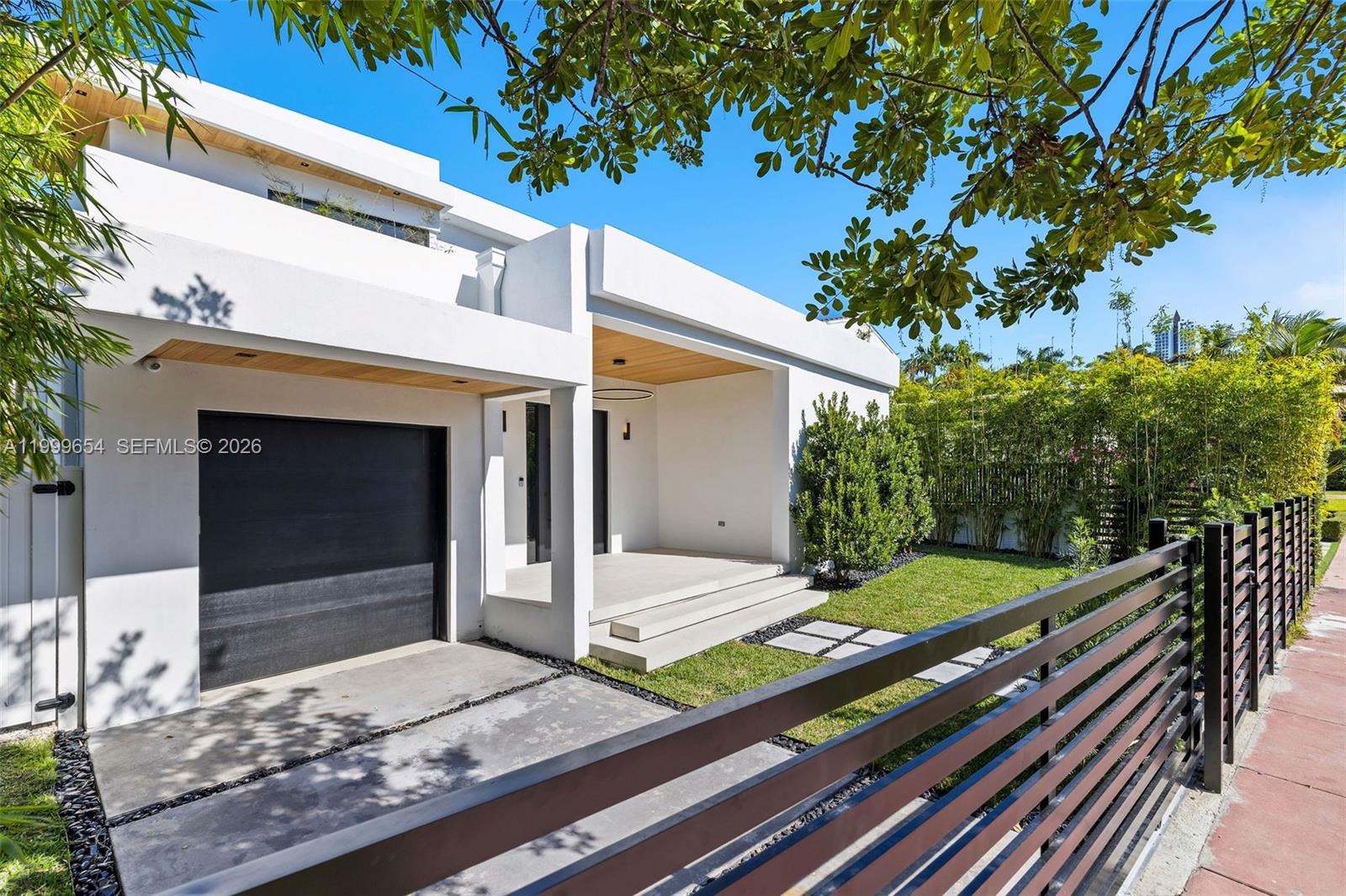 A modern white house features a black garage door, wood-paneled ceiling, and a metal fence — 325 W 63rd St, Miami Beach FL 33141, MIAMI BEACH, FL