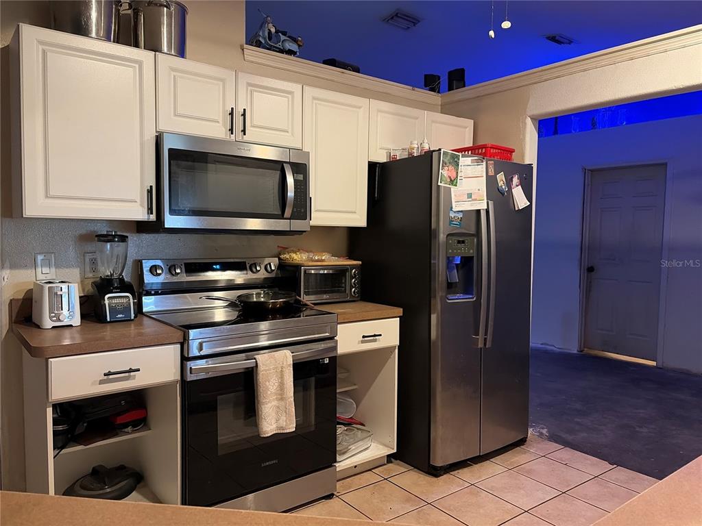 A kitchen features white cabinets, stainless steel appliances, and tile flooring — 1104 67TH AVENUE W, BRADENTON, FL