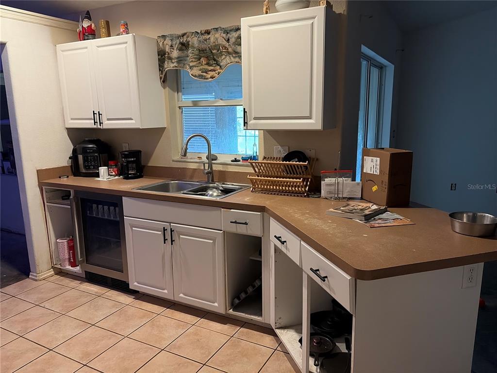 A kitchen features white cabinets, a brown countertop, a double sink, and tiled flooring — 1104 67TH AVENUE W, BRADENTON, FL