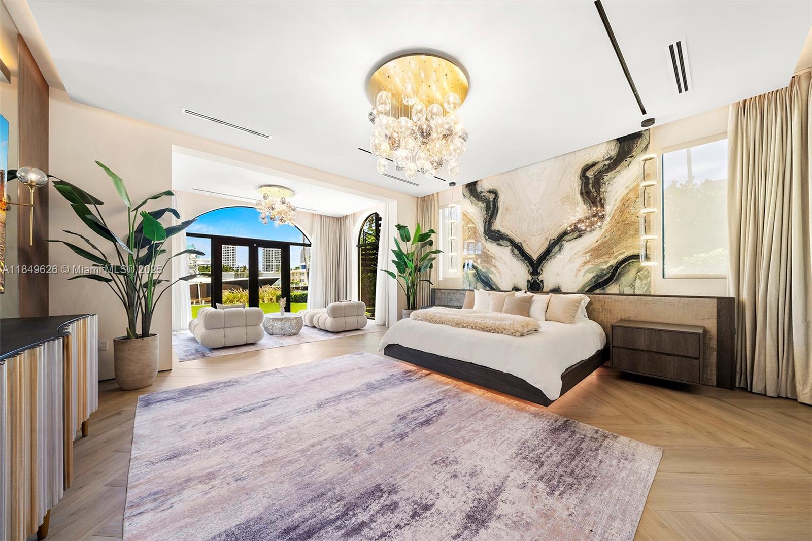 A spacious bedroom features a large bed against a marble wall and a seating area — FORT LAUDERDALE, FL