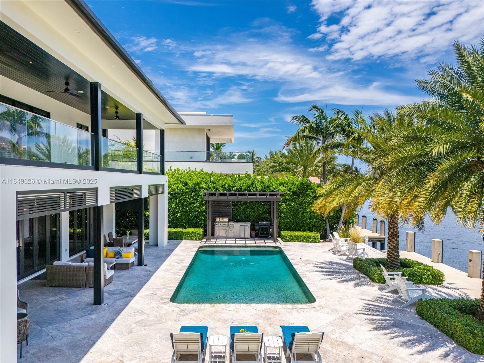 A modern waterfront home features a swimming pool, outdoor kitchen, and patio with lounge chairs — FORT LAUDERDALE, FL