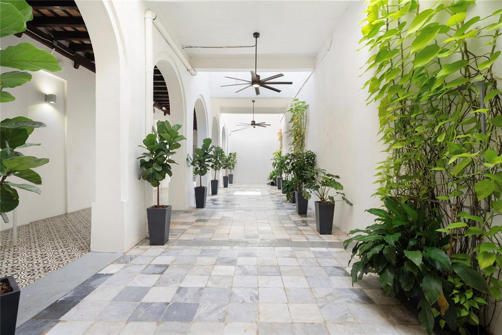 A long, open-air hallway features arched doorways, tiled flooring, ceiling fans, and potted plants — 205 LUNA, OLD SAN JUAN, PR