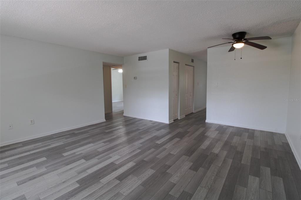 An empty living room features gray wood-look flooring, white walls, and a ceiling fan — 201 POINSETTIA PINE COURT UNIT 202, TAMPA, FL