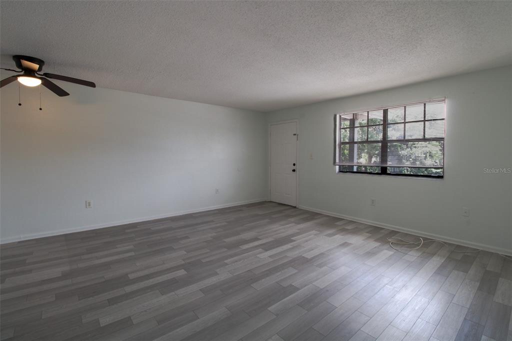 An empty room features light gray walls, wood-look flooring, a ceiling fan, and a window — 201 POINSETTIA PINE COURT UNIT 202, TAMPA, FL