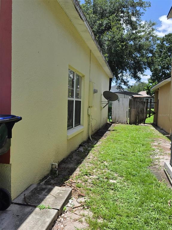 A side view of a yellow stucco house exterior with a grassy yard and fence — 2261 BLUE SAPPHIRE CIRCLE, ORLANDO, FL
