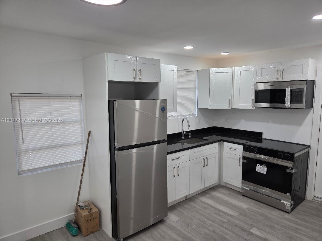 A kitchen features white cabinets, stainless steel appliances, black countertops, and light wood-look flooring — 2911 NW 30th St, Miami FL 33142, MIAMI, FL
