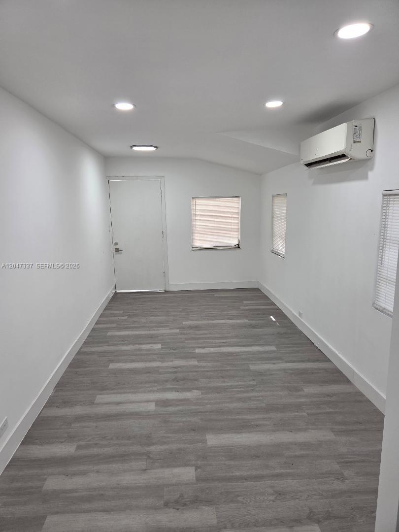 A minimalist room features light gray wood-look flooring, white walls, recessed lighting, and a wall-mounted AC — 2911 NW 30th St, Miami FL 33142, MIAMI, FL