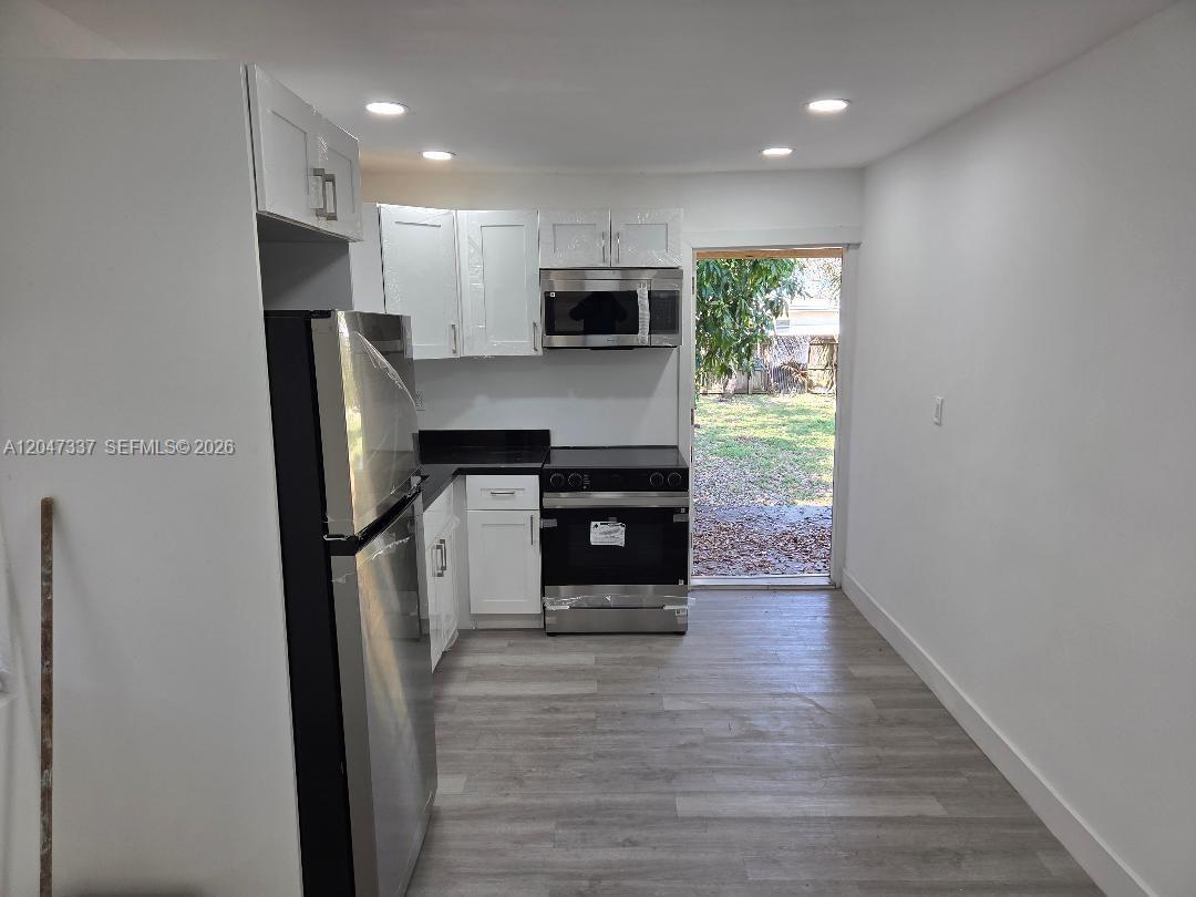A kitchen features white cabinets, stainless steel appliances, and light wood-look flooring — 2911 NW 30th St, Miami FL 33142, MIAMI, FL