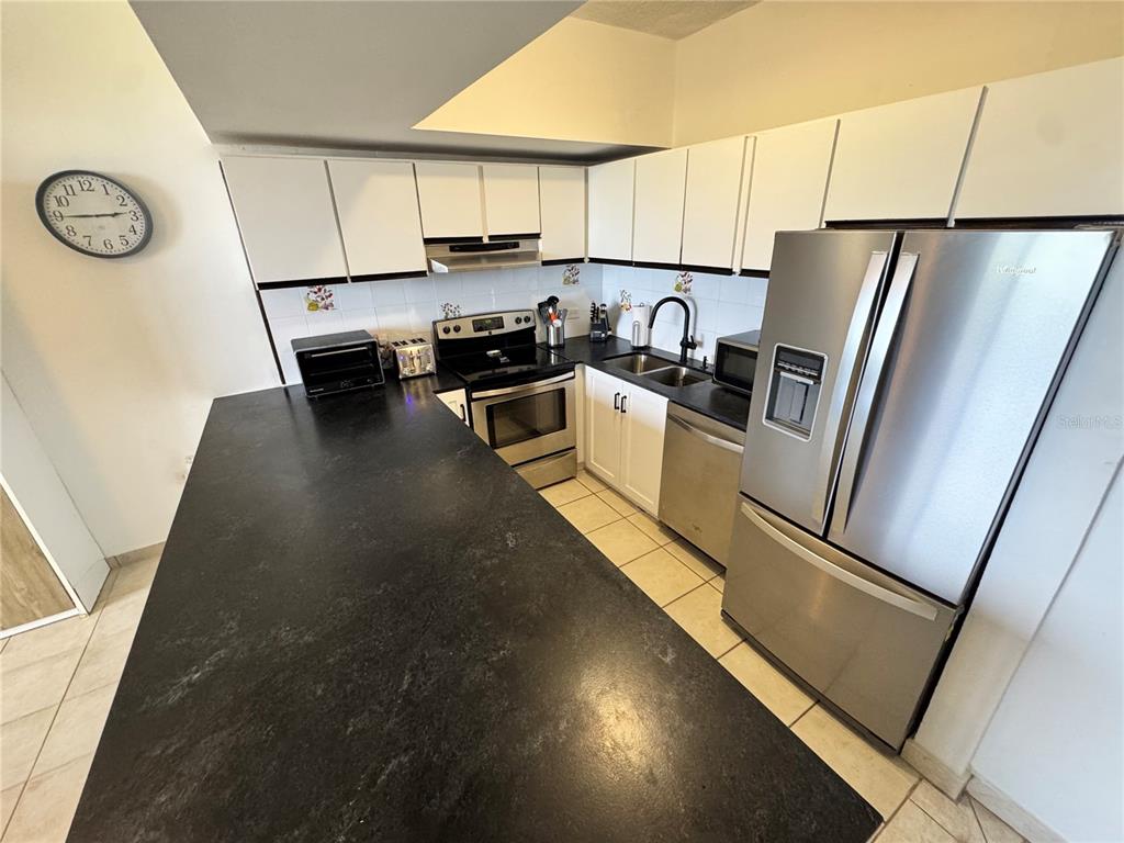 A kitchen features white cabinets, black countertops, stainless steel appliances, and a large island — 222 BEACH VILLAGE, HUMACAO, PR