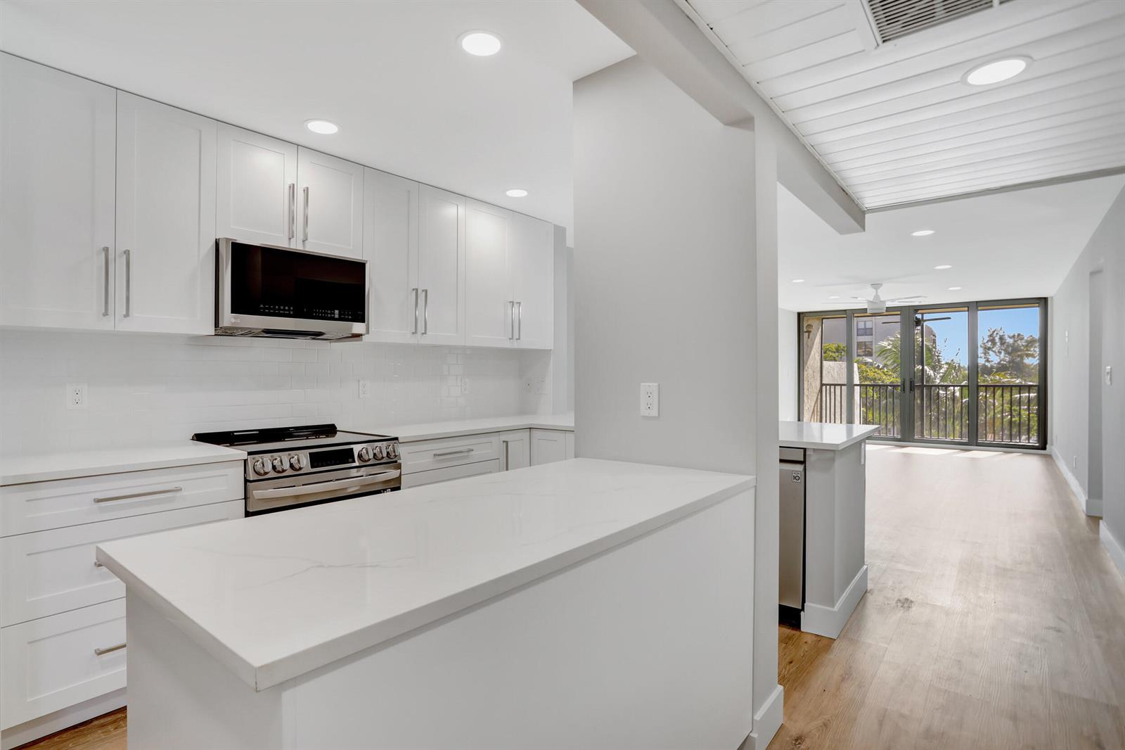A modern kitchen with white cabinets, quartz countertops, and stainless steel appliances overlooks a balcony — 7 Royal Palm Way # 404, Boca Raton FL 33432, BOCA RATON, FL