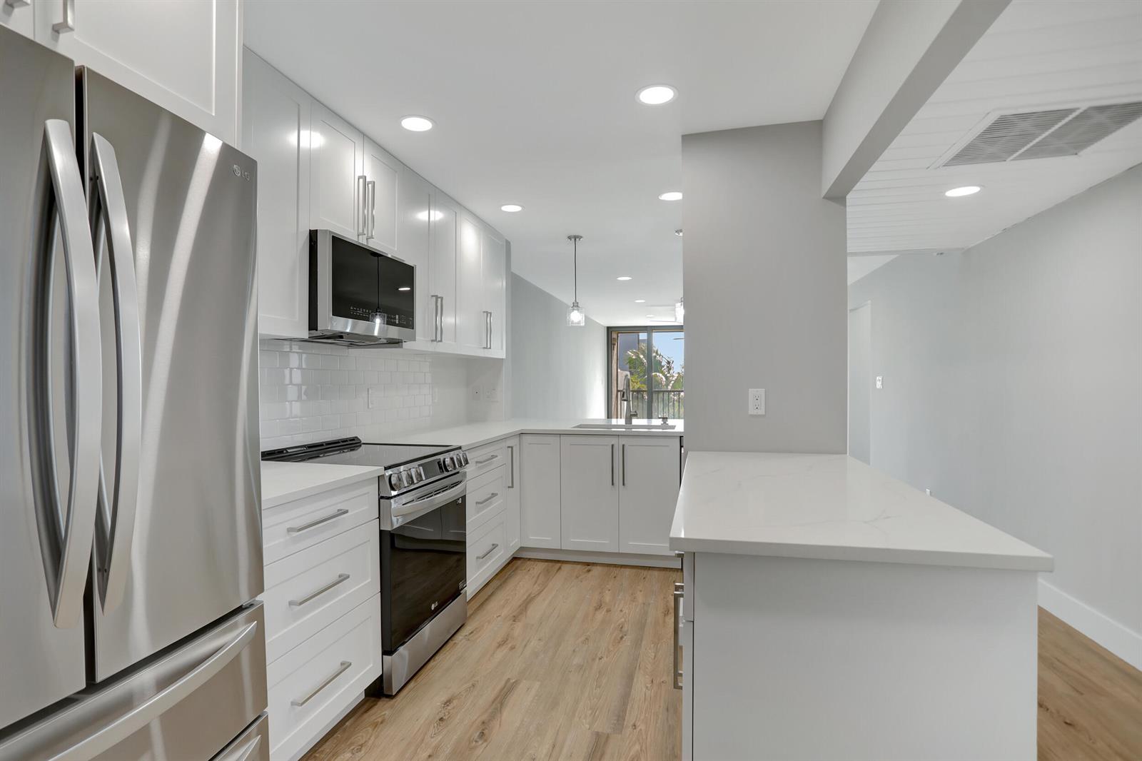 A modern kitchen features white cabinetry, stainless steel appliances, quartz countertops, and light wood flooring — 7 Royal Palm Way # 404, Boca Raton FL 33432, BOCA RATON, FL