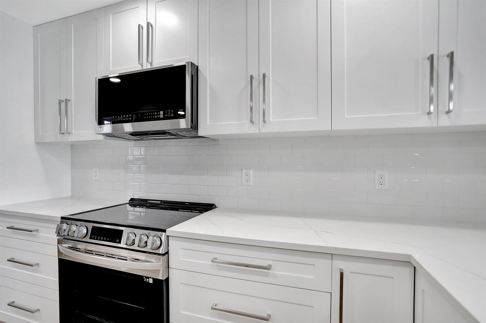 A modern kitchen features white shaker cabinets, stainless steel appliances, and white subway tile backsplash — 7 Royal Palm Way # 404, Boca Raton FL 33432, BOCA RATON, FL