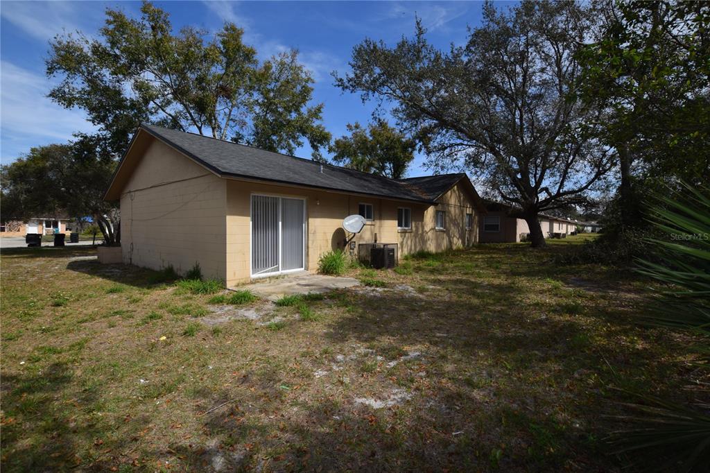 The exterior of a tan concrete block house features a sliding glass door and yard — 3264 SPLIT WILLOW DRIVE, ORLANDO, FL