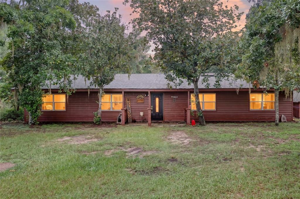A single-story house with brown wood siding and a black front door sits among trees — 35446 FOURAKER DRIVE, FRUITLAND PARK, FL