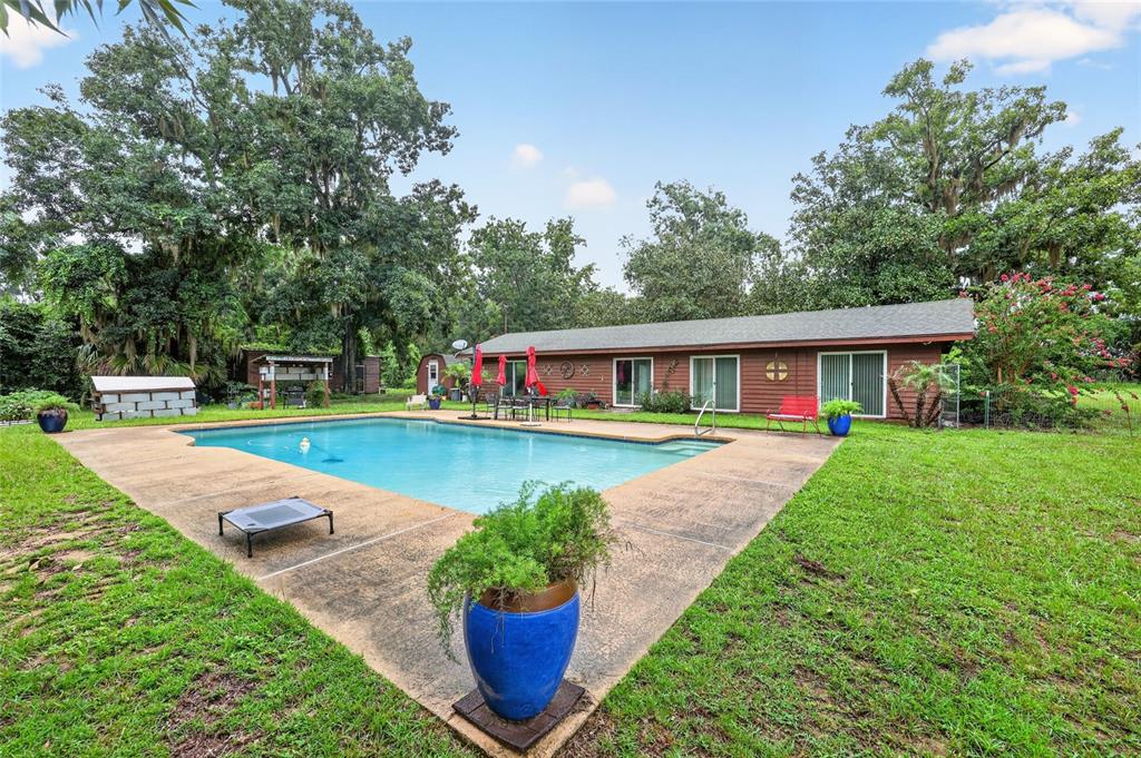 A backyard features a rectangular swimming pool, a concrete patio, and a single-story brown house — 35446 FOURAKER DRIVE, FRUITLAND PARK, FL
