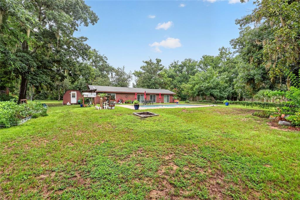 A backyard with a swimming pool, a small shed, and a fire pit on grass — 35446 FOURAKER DRIVE, FRUITLAND PARK, FL