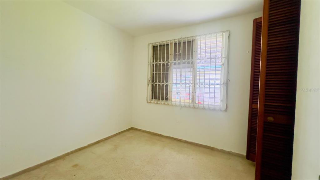 An empty bedroom features plain white walls, beige carpeting, and a window with security bars — #9 CALLE REPARTO GONZALEZ, AGUADA, PR
