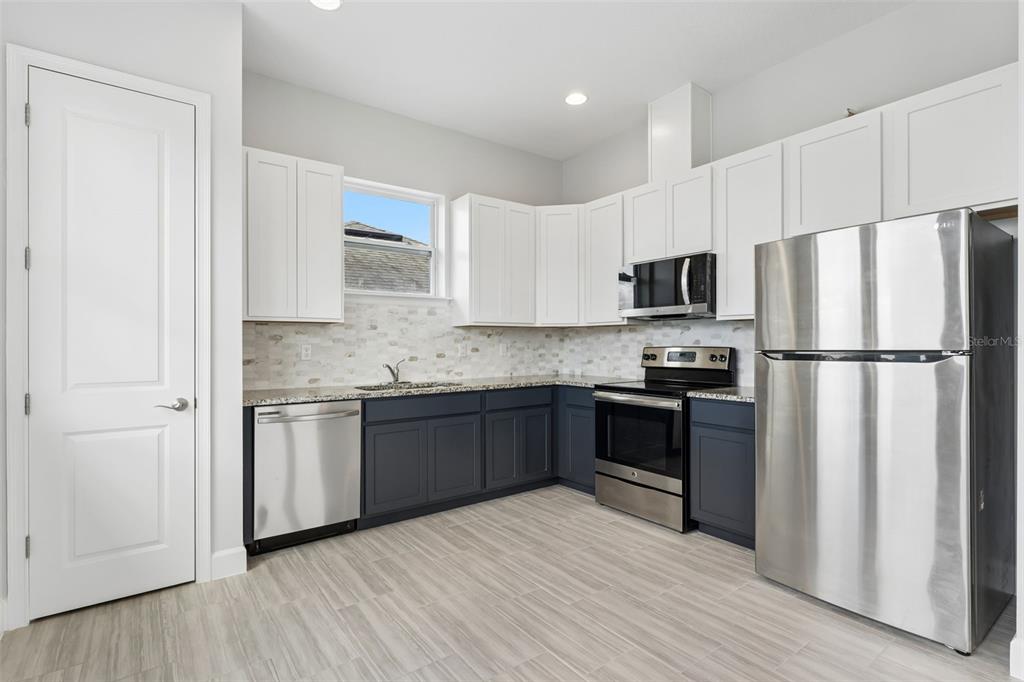 A carpeted room with a ceiling fan, three windows, and a small kitchenette in the corner — 8033 NEMOURS PARKWAY, ORLANDO, FL