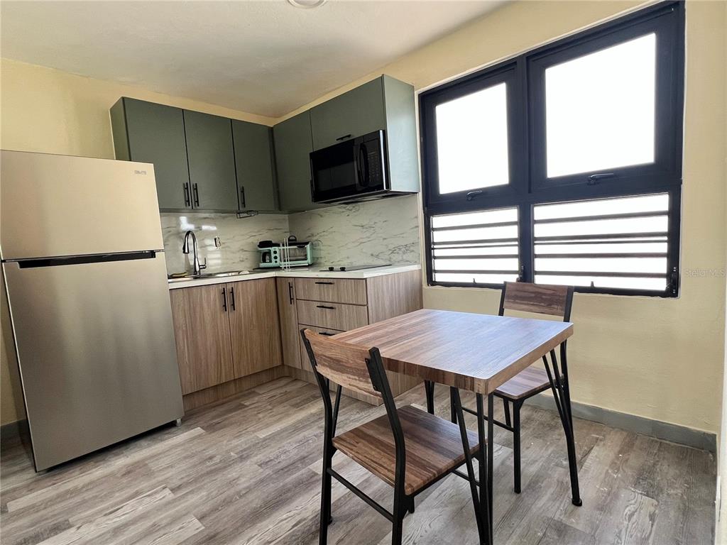 A kitchen features green upper cabinets, wood-look lower cabinets, stainless steel appliances, and a dining set — 84  ST. URB SIERRA BAYAMON 98-1 APT. #7, BAYAMON, PR