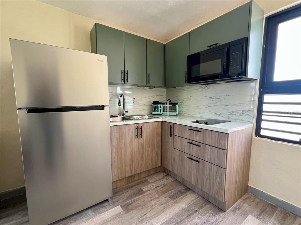 A small kitchen features green upper cabinets, wood-grain lower cabinets, stainless steel appliances, and marble-look backsplash — 84  ST. URB SIERRA BAYAMON 98-1 APT. #7, BAYAMON, PR
