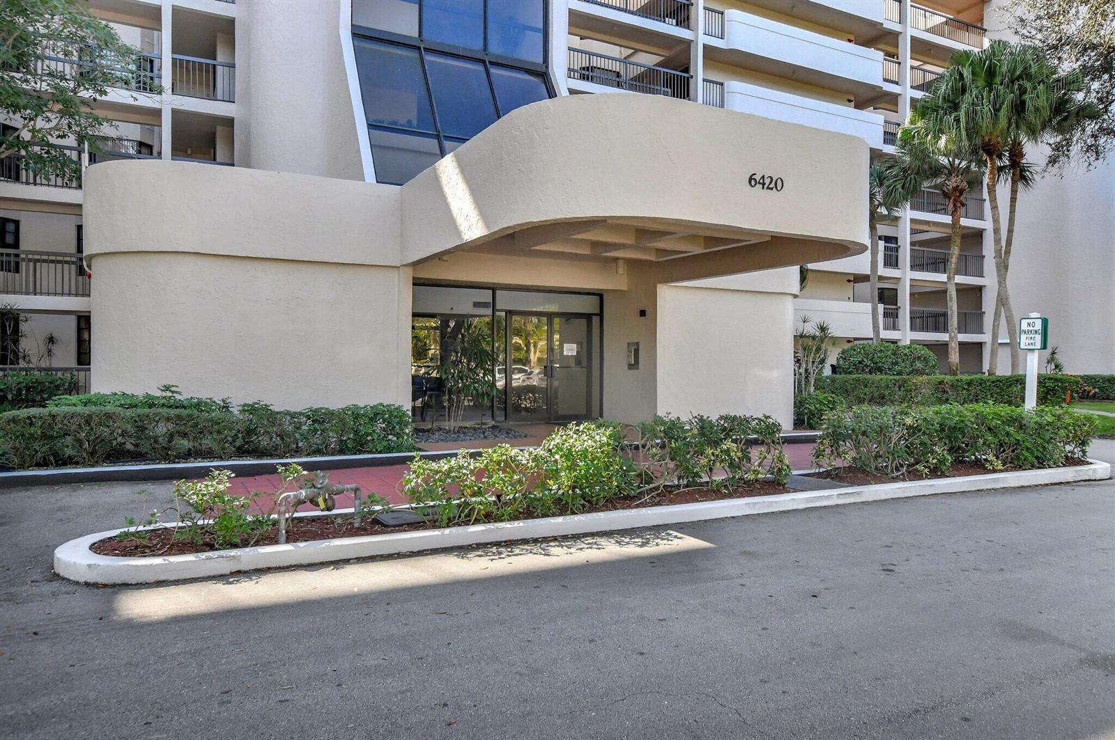 The exterior entrance of a multi-story building features a curved concrete overhang and glass doors — 6420 Boca Del Mar # 303, Boca Raton FL 33433, BOCA RATON, FL