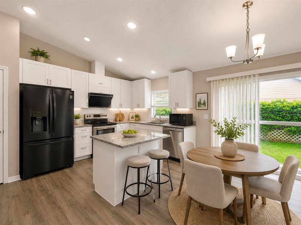 A kitchen with white cabinets, granite countertops, a center island, and an adjacent dining area — 28427 SUNVALE PLACE, WESLEY CHAPEL, FL