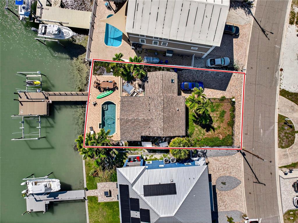 An aerial view shows a waterfront house with a pool, dock, and paved driveway — 449 S BAYSHORE DRIVE, MADEIRA BEACH, FL