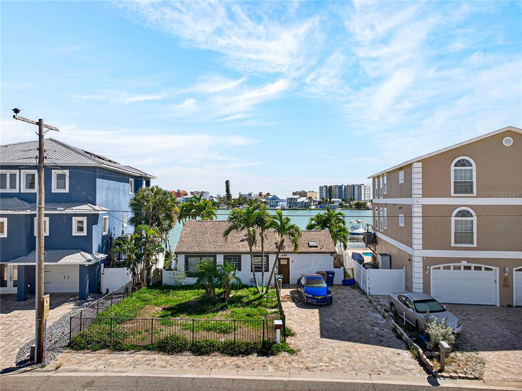 A single-story house sits between two taller multi-story homes along a waterfront canal — 449 S BAYSHORE DRIVE, MADEIRA BEACH, FL