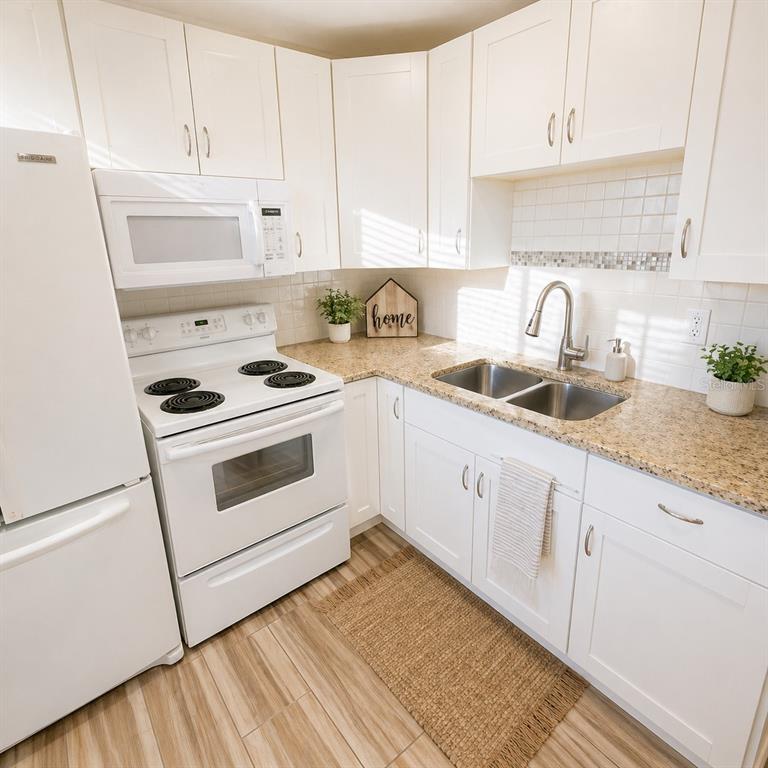 A kitchen features white cabinets, granite countertops, a white electric stove, and a double sink — 2501 HARN BOULEVARD UNIT H27, CLEARWATER, FL