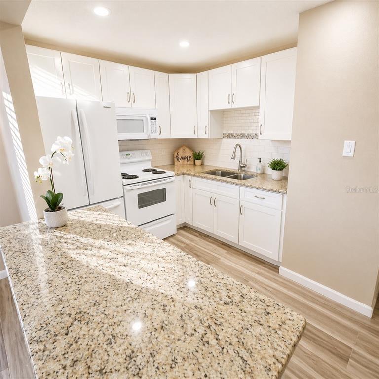 A kitchen features white cabinets, granite countertops, stainless steel appliances, and light wood-look flooring — 2501 HARN BOULEVARD UNIT H27, CLEARWATER, FL