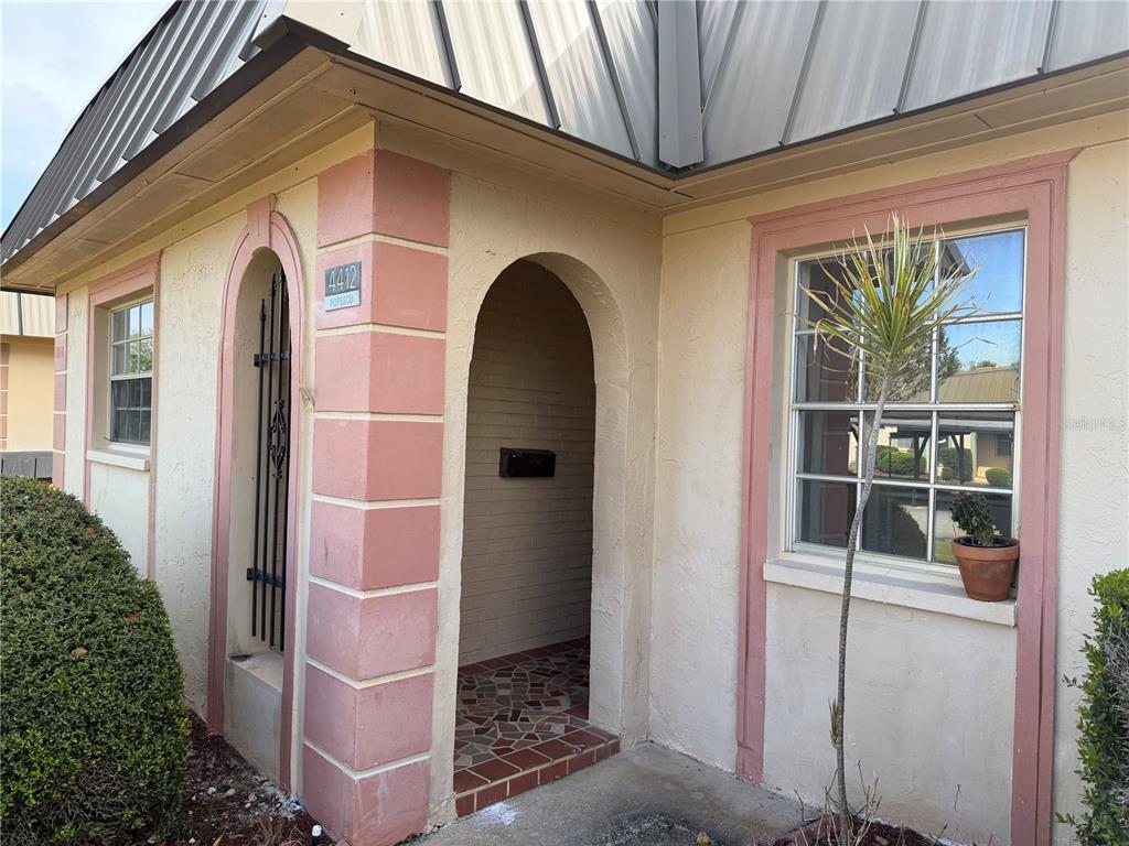 The exterior of a building features a recessed arched entryway, pink trim, and a metal roof — 4412 SUNSTATE DRIVE UNIT A, NEW PORT RICHEY, FL