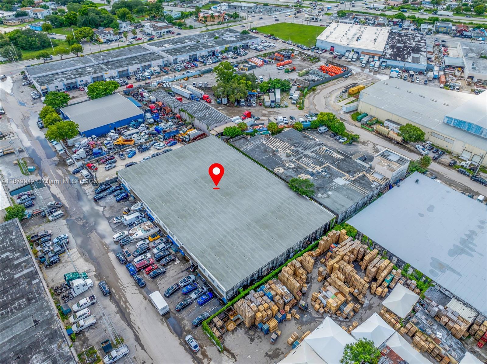 An aerial view shows a large industrial warehouse building surrounded by parked vehicles and pallets — 2310 NW 150th St, Opa-Locka FL 33054, OPA-LOCKA, FL