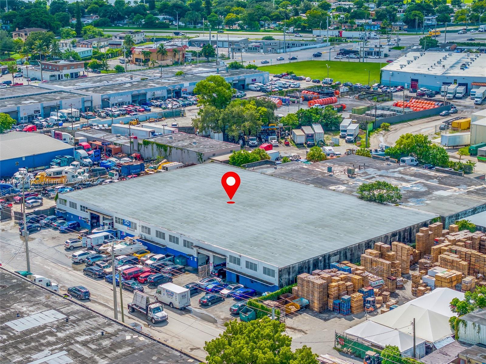 An aerial view shows a large industrial warehouse building with a parking lot and pallets — 2310 NW 150th St, Opa-Locka FL 33054, OPA-LOCKA, FL