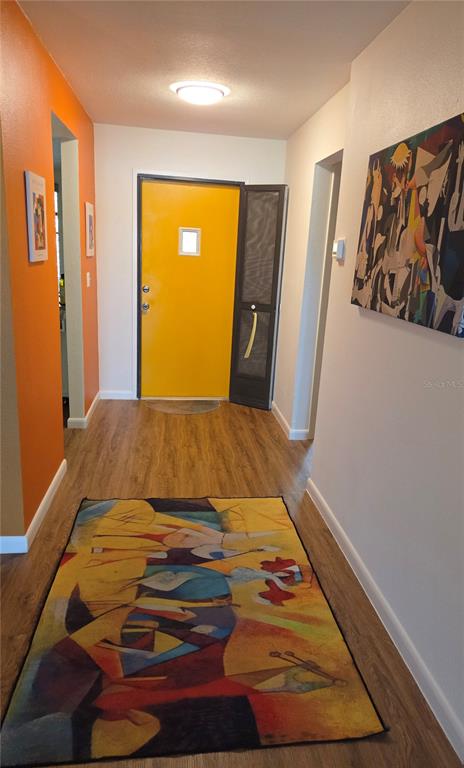An entryway features a bright yellow front door, wood-look flooring, and colorful abstract wall art — 4416 SPICEWOOD DRIVE UNIT J, BRADENTON, FL