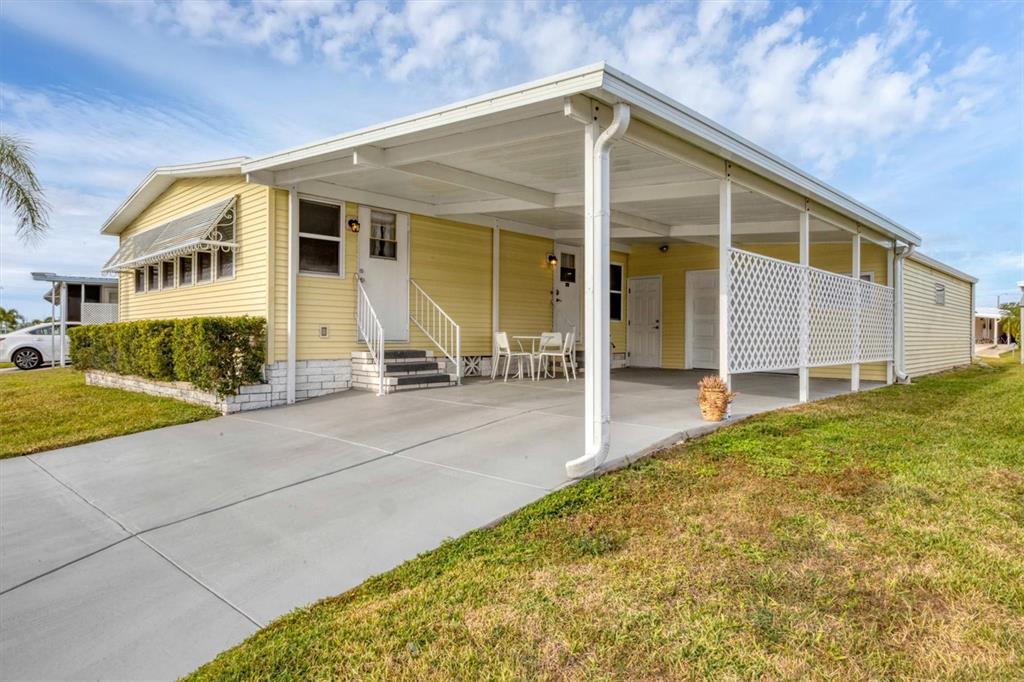 A yellow mobile home features a concrete driveway, a covered carport, and a small patio — 4532 12TH STREET COURT E, ELLENTON, FL